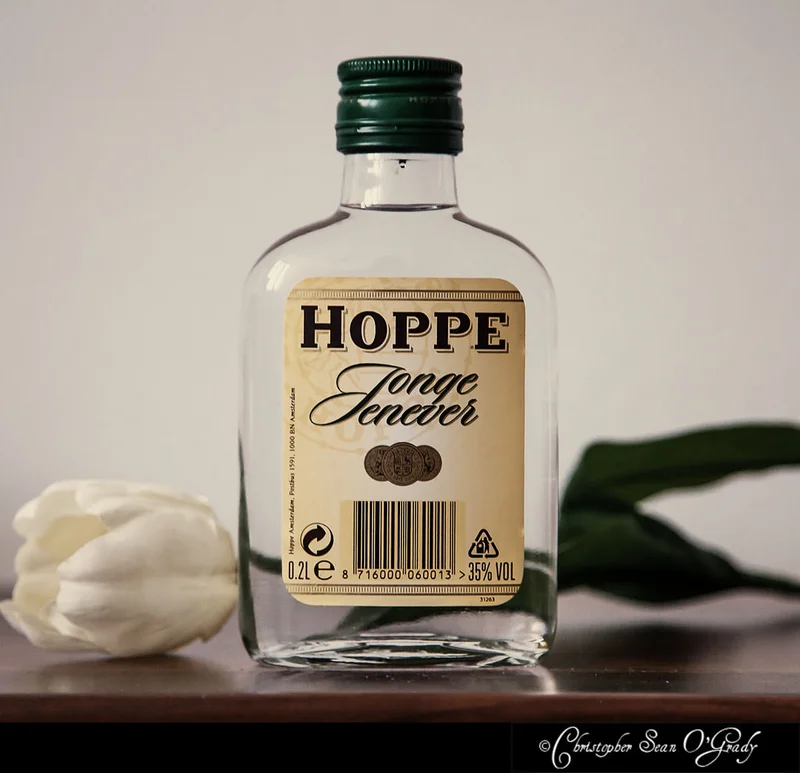Hoppe Jonge Jenever bottle on a wooden shelf with a white tulip