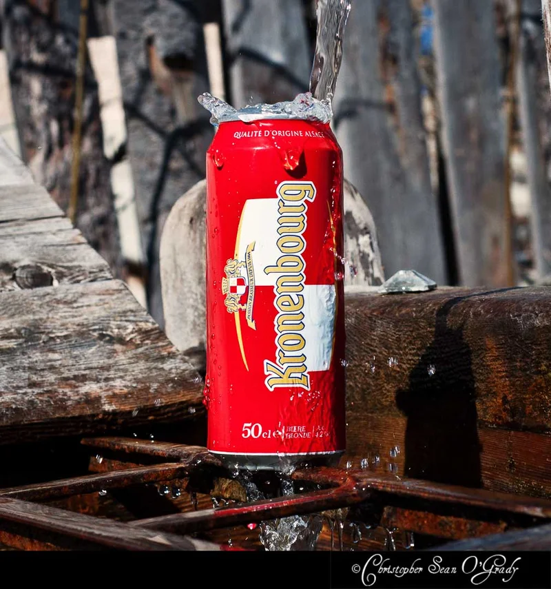 Kronenbourg can with water pouring over it on a rustic wooden surface