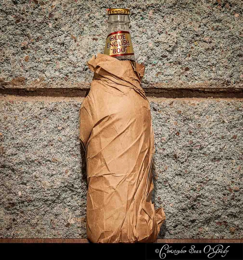 Olde English 800 malt liquor bottle in a brown paper bag against concrete wall