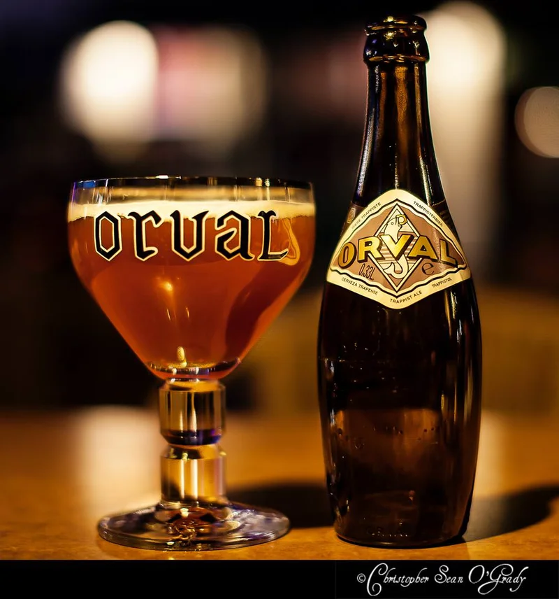Orval Trappist ale bottle with branded chalice glass at a dimly lit bar