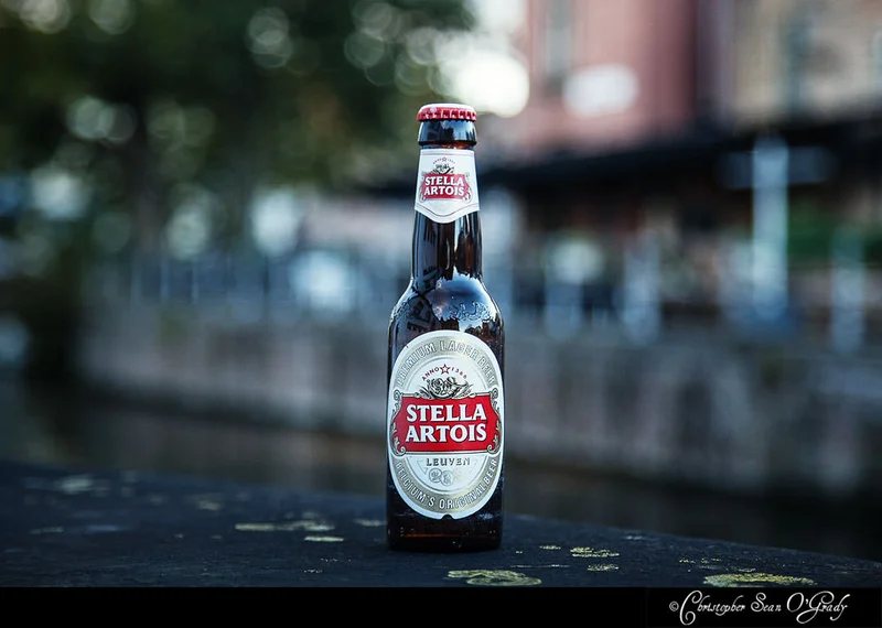 Stella Artois beer bottle on a canal bridge ledge with blurred city backdrop