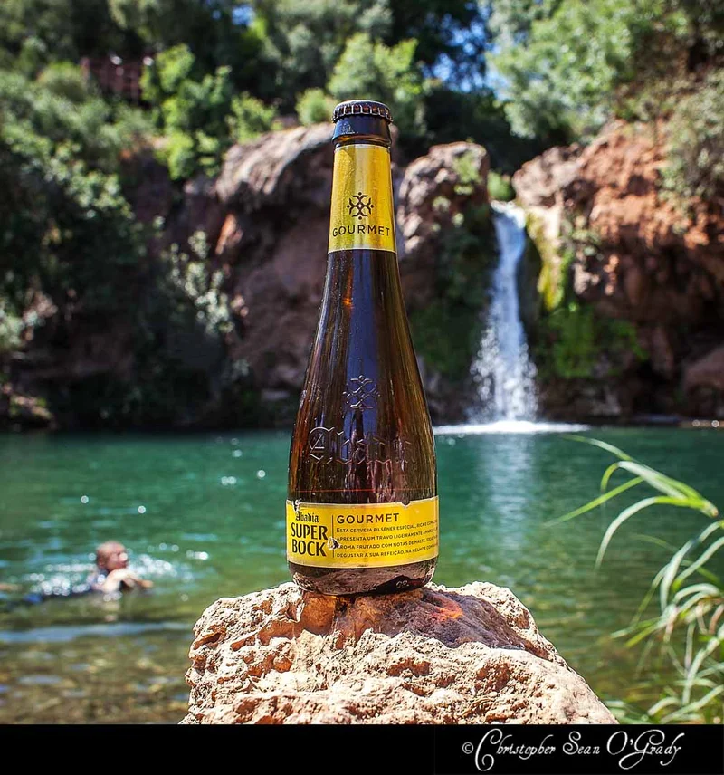 Super Bock Abadia Gourmet beer bottle on a rock at a waterfall swimming hole