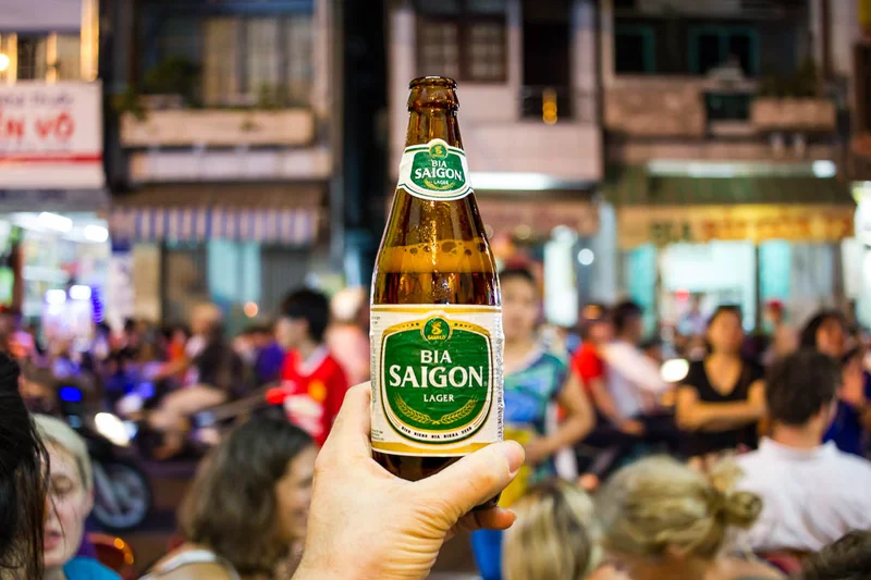 Bia Saigon Lager bottle held up at a bustling Vietnamese street scene at night