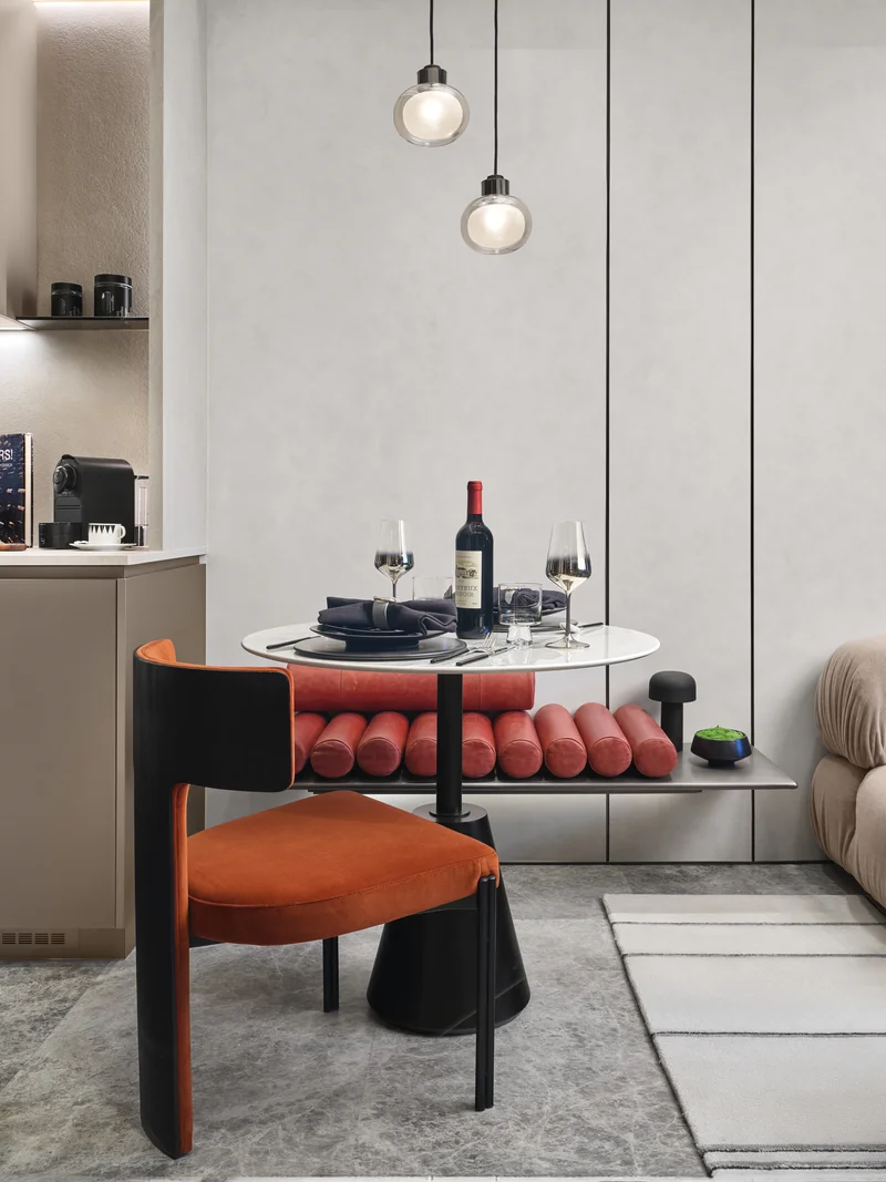 Private residential 1-bedroom showflat dining nook and kitchen with round table, red bench and compact cabinetry, detail view