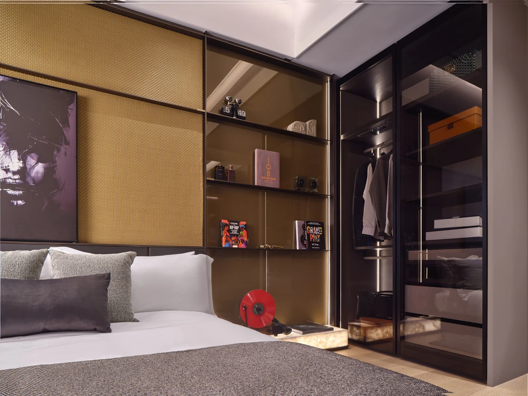 W Residences 1-bedroom showflat bedroom with open wardrobe shelving, upholstered bed and warm lighting, wide view