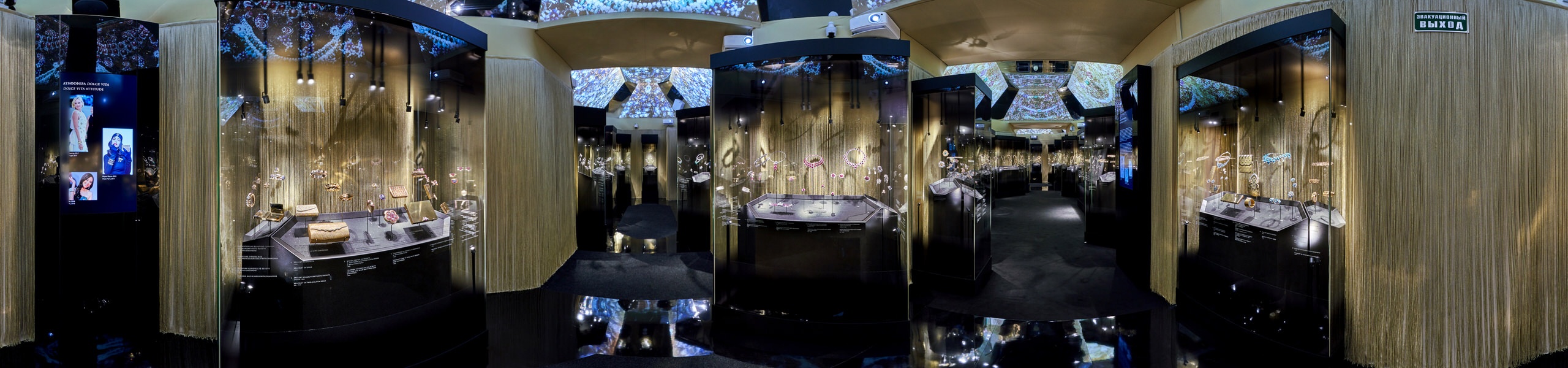 Panoramic view of opulent jewellery gallery with gold chain curtains, glass display cases, projected ceiling patterns, and video screen