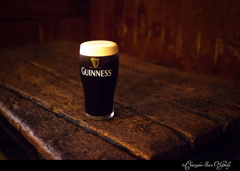 Guinness pint with creamy head on a rustic wooden table in a dimly lit pub