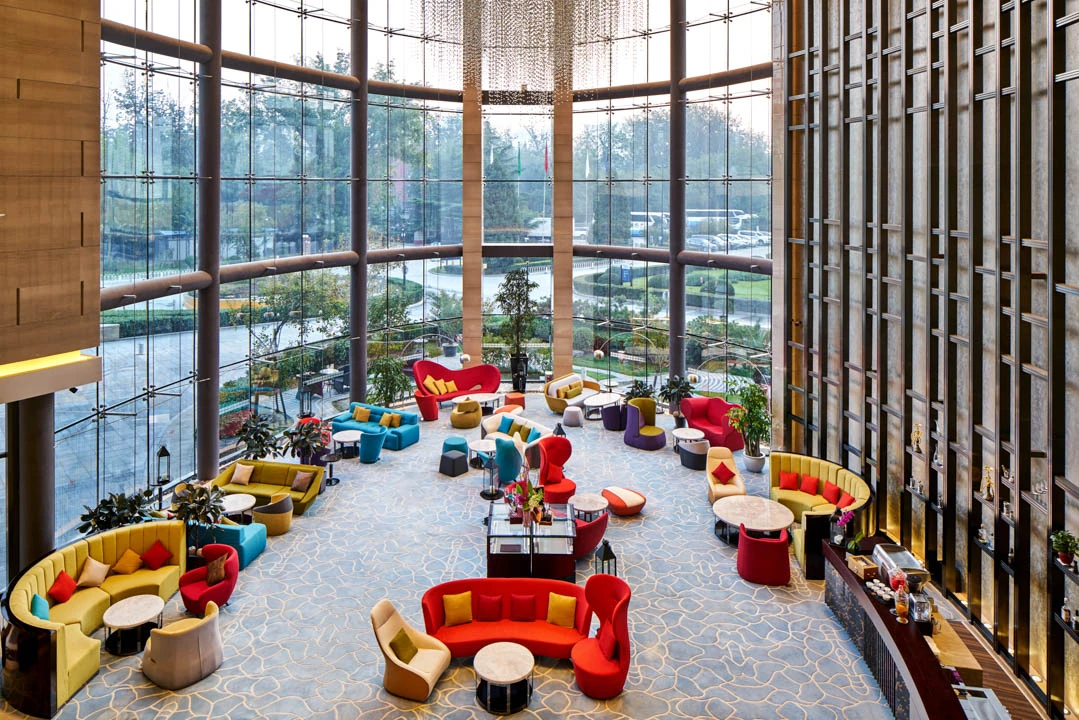 Double-height lobby with colourful sofas, crystal curtain chandelier and curved glass walls — Crowne Plaza Beijing Lido hospitality photography