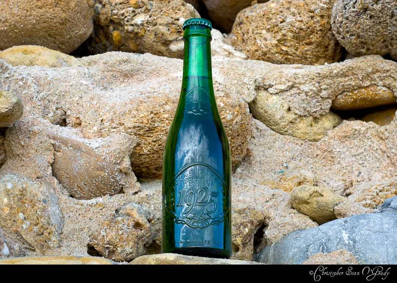 Alhambra Reserva 1925 green bottle nestled among sandy coastal rocks