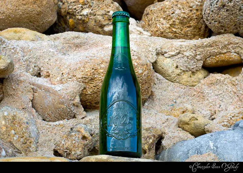 Alhambra Reserva 1925 green bottle nestled among sandy coastal rocks