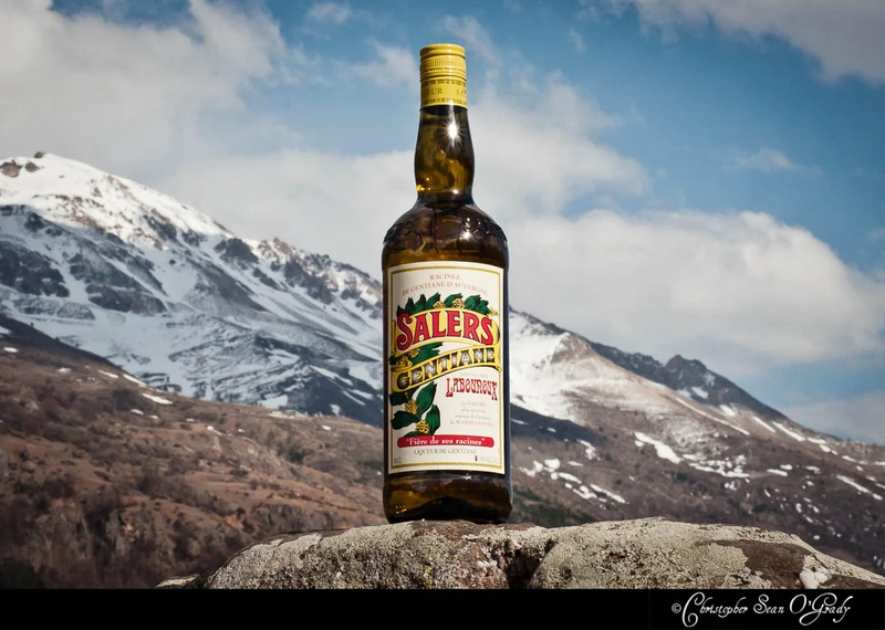 Salers Gentiane liqueur on a stone ledge with snow-capped mountains behind