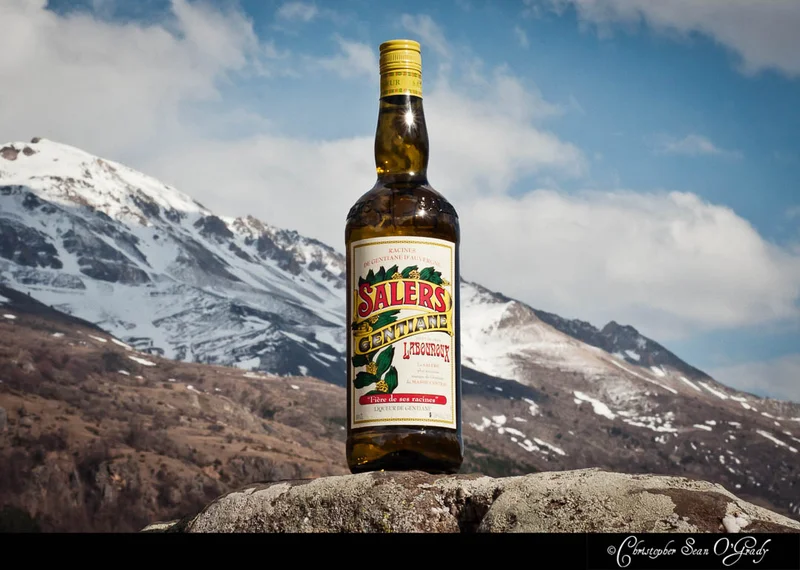Salers Gentiane liqueur on a stone ledge with snow-capped mountains behind