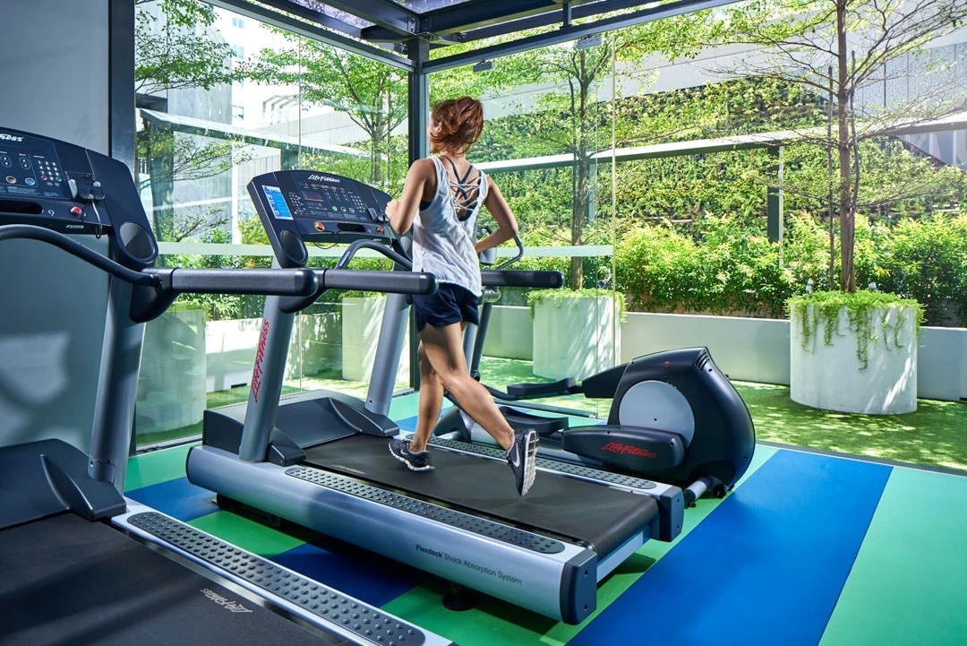 Woman running on treadmill in glass-walled fitness centre with garden view