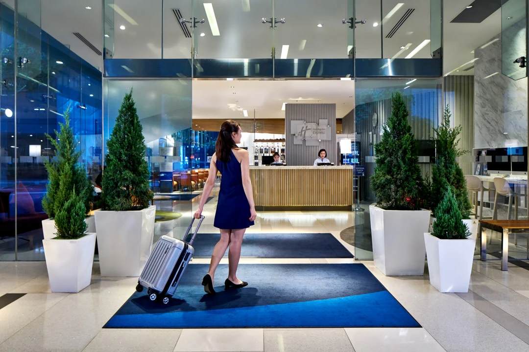 Guest arriving at glass entrance with rolling suitcase at dusk