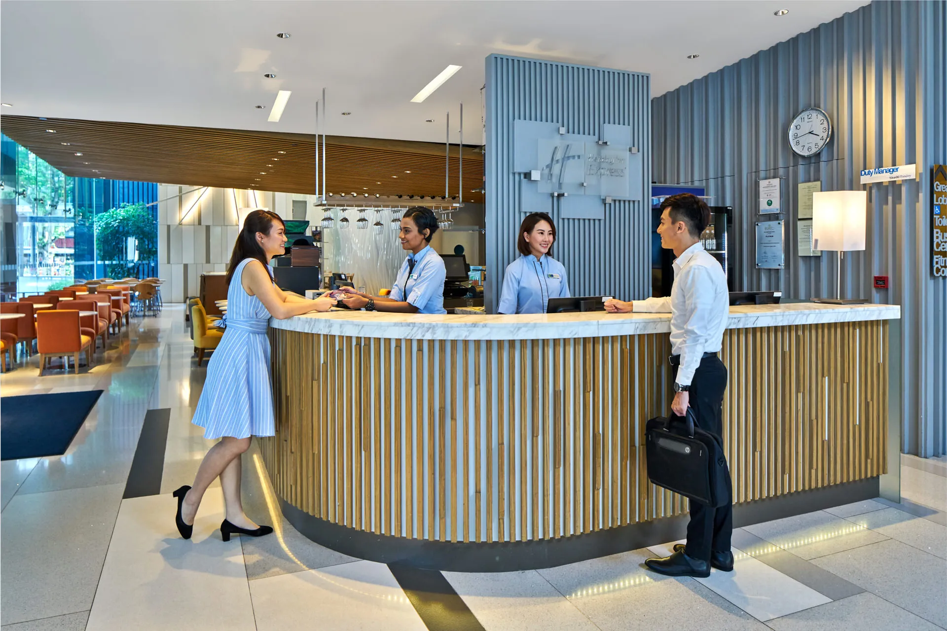 Staff assisting guests at curved reception desk in hotel lobby — Holiday Inn Express Orchard hospitality photography