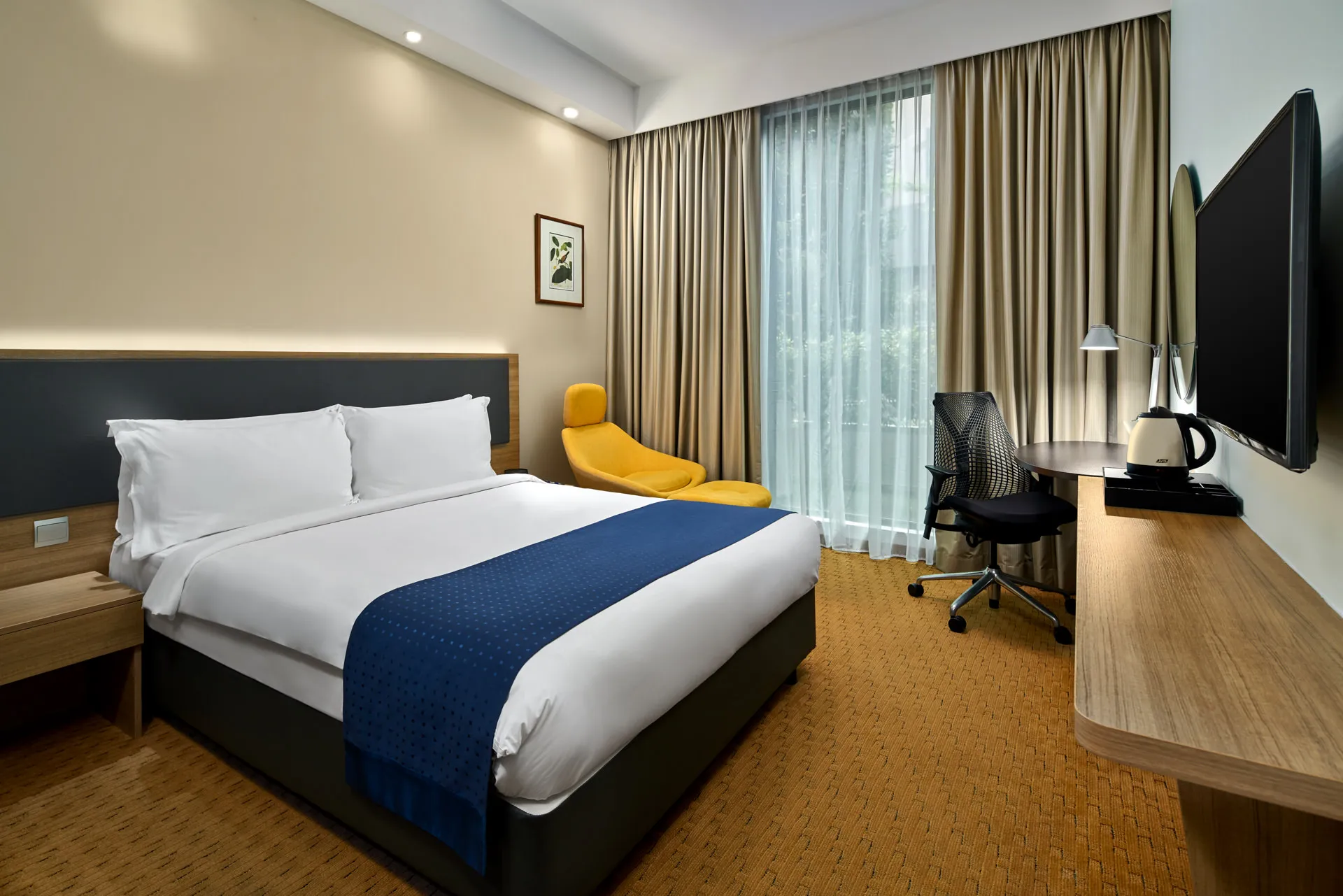 Queen room with yellow accent chair, work desk and warm lighting — Holiday Inn Express Orchard hotel photography