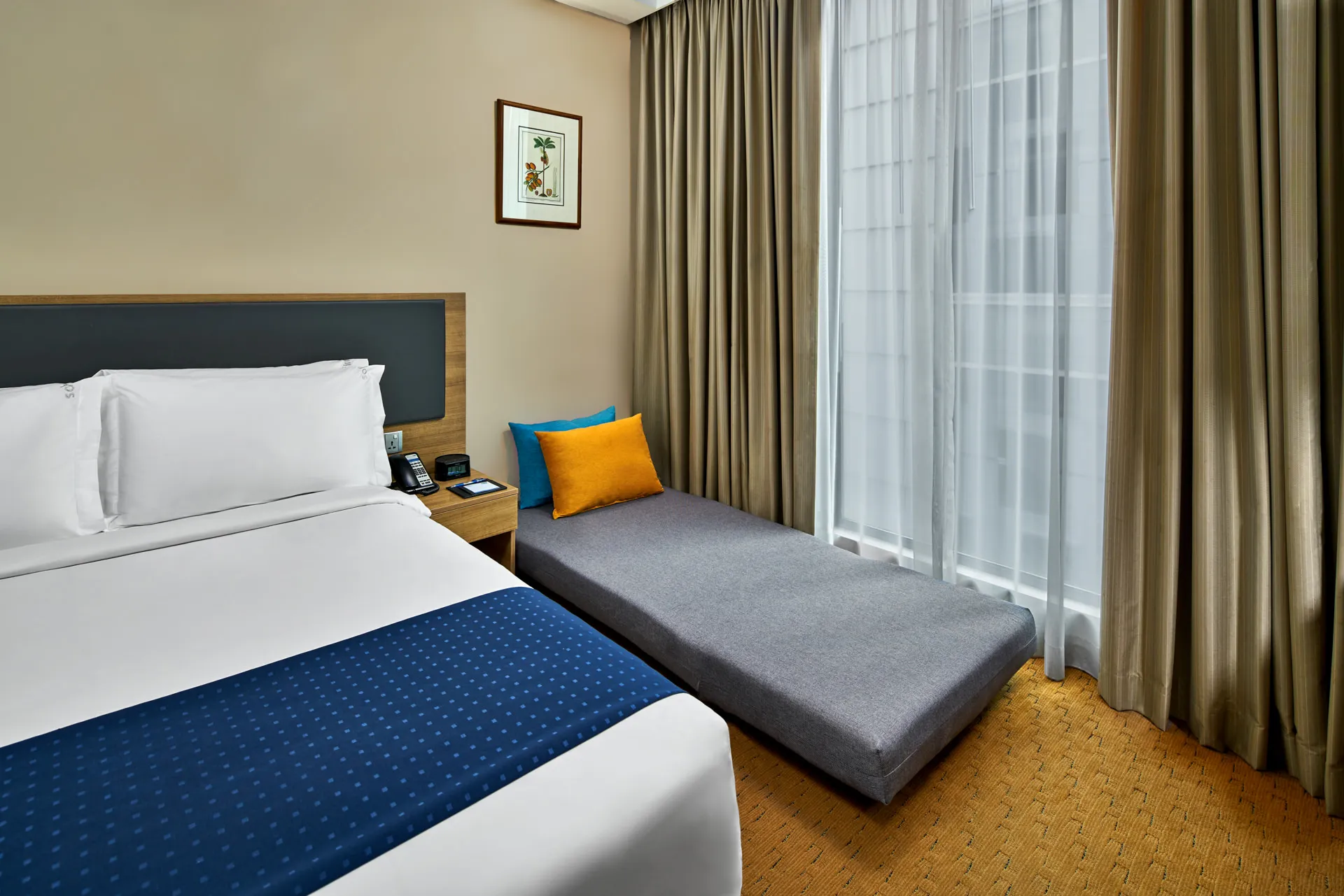 Queen bed beside grey daybed with teal cushions and botanical print — Holiday Inn Express Orchard interior photography