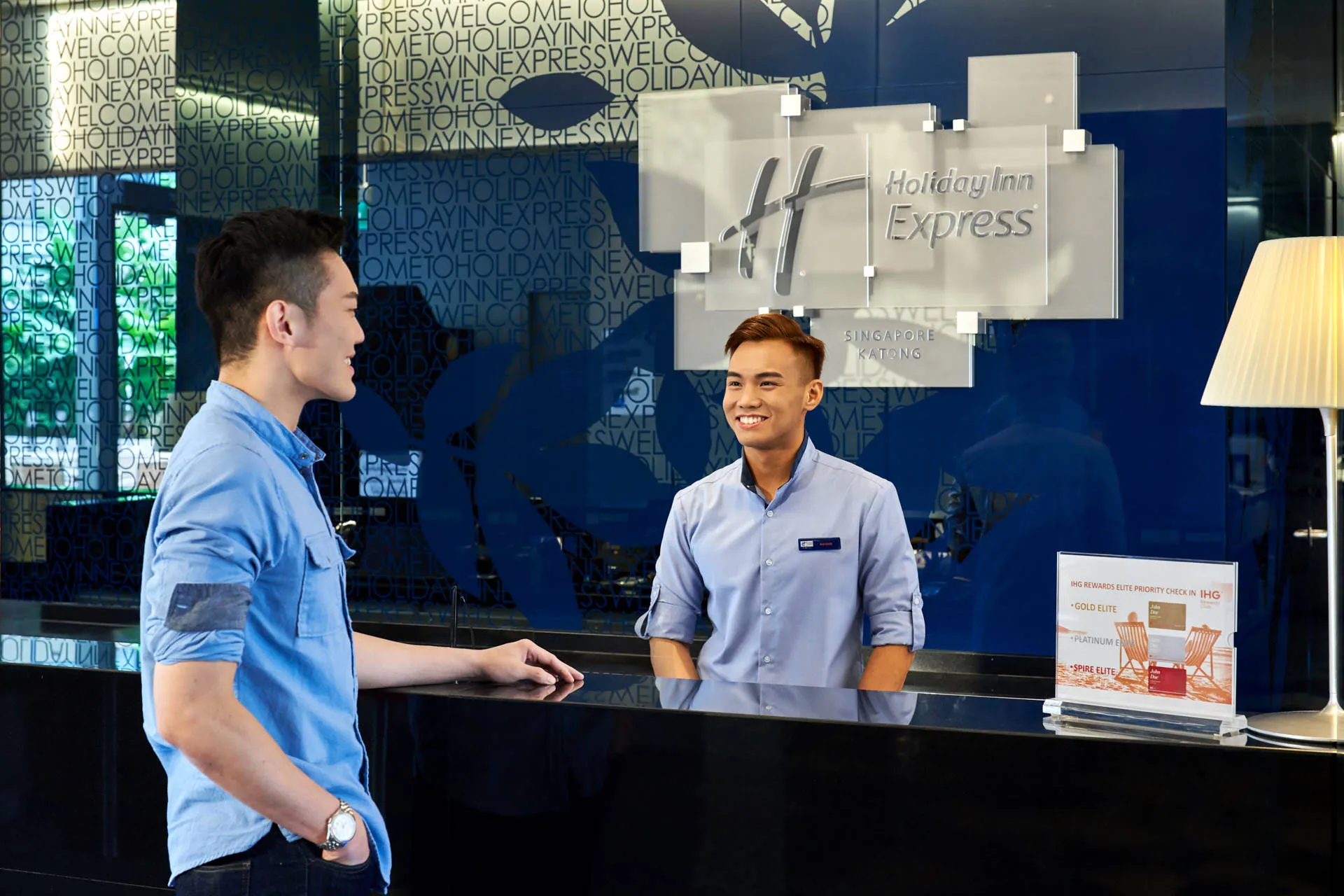 Staff greeting guest at reception with branded blue backdrop — Holiday Inn Express Katong hospitality photography