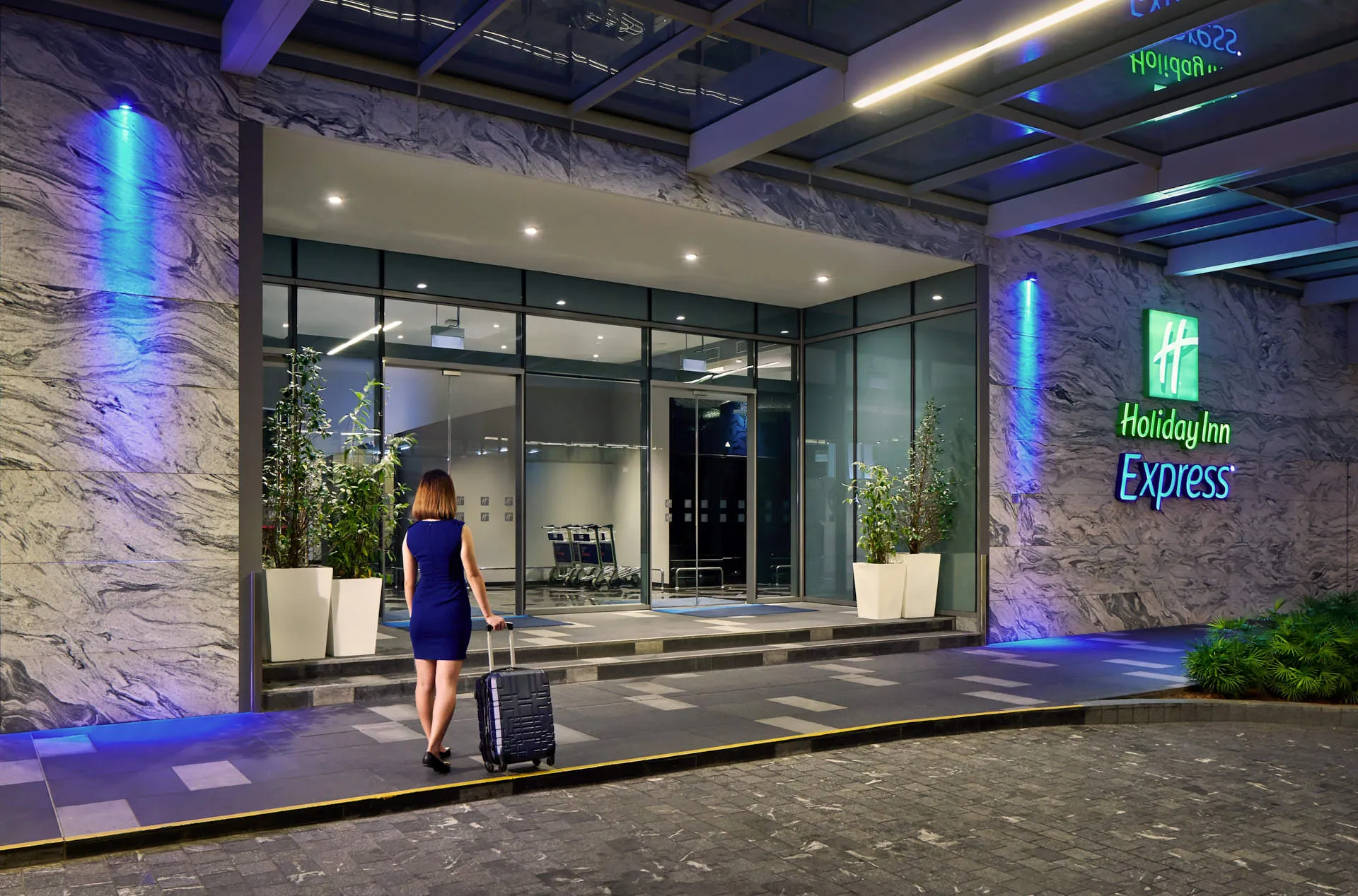 Guest arriving at hotel entrance with luggage under blue accent lighting — Holiday Inn Express Katong hotel photography