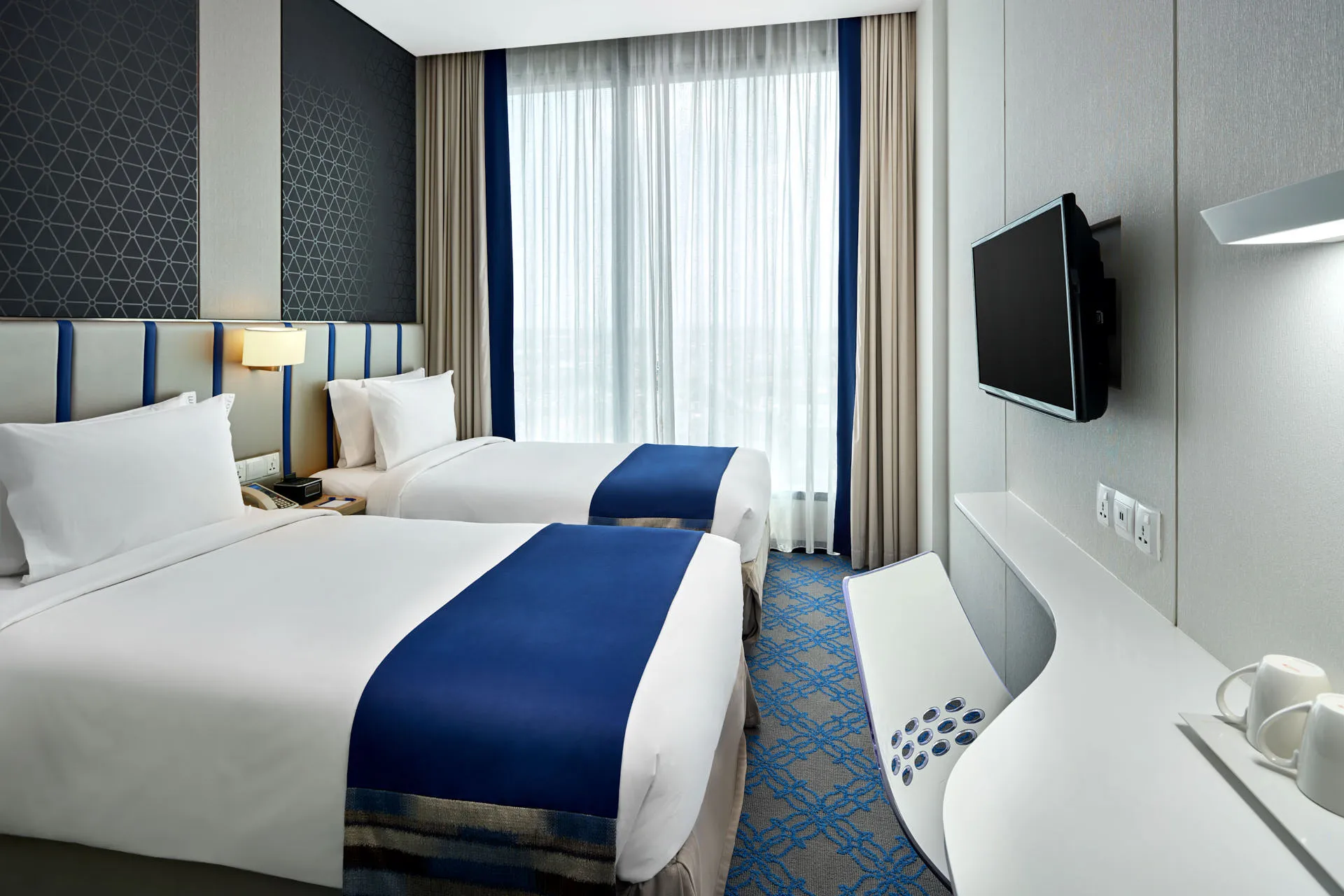 Twin room with blue runners, geometric accent wall and warm lighting — Holiday Inn Express Katong interior photography