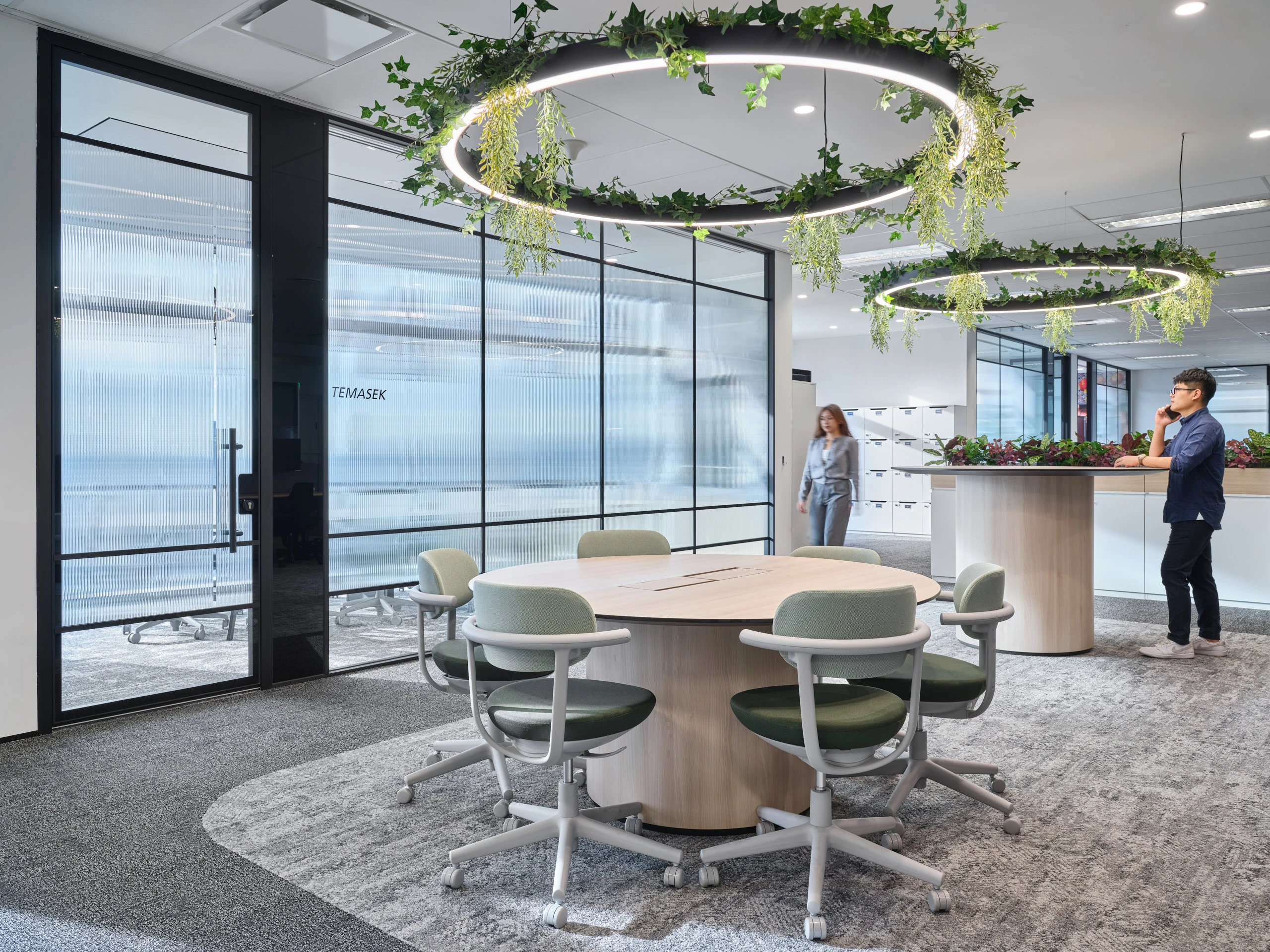 Collaborative zone with green chairs, planter islands and LED ring chandeliers
