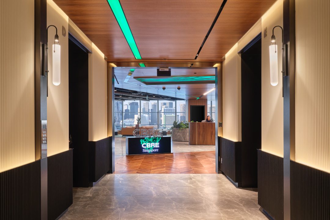 Modern office entrance hallway with wood slat walls leading to a bright, open-plan lounge, showcasing professional workplace photography in Singapore.